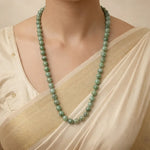 Person wearing a green beaded necklace with a beige top