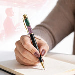 Hand holding a decorative pen with gemstone accents on a light surface.