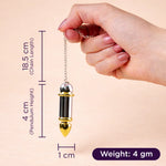 Hand holding a gold pendulum with measurements on a beige background