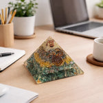 Pyramid-shaped decorative item on a desk with laptop, notebook, and cup in the background