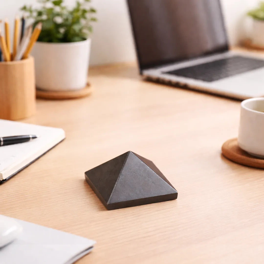 Pyramid-shaped object on a desk with laptop, notebook, and cup in the backgroundPyrite Small Pyramid – Wealth Attraction & Protection Crystal