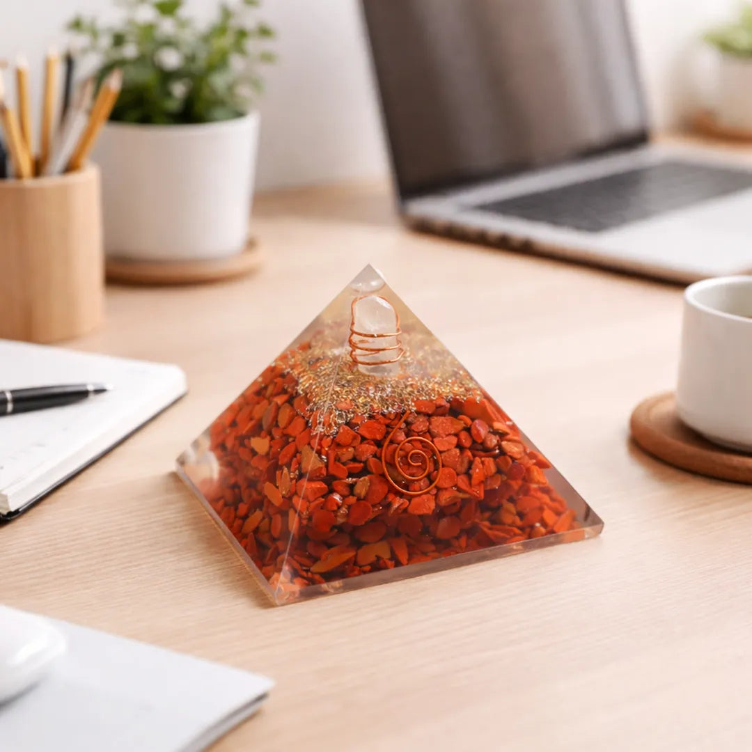 Pyramid-shaped object with red stones on a desk with laptop and office supplies