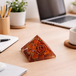Pyramid-shaped decorative object on a desk with a laptop, notebook, and cup in the background.