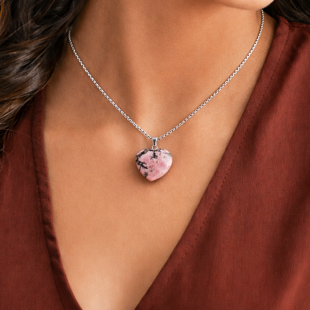 Necklace with a pink heart-shaped pendant worn by a person in a brown top.