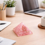 Pink pyramid-shaped object with a spiral design on a desk with a laptop and office supplies.