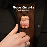 Rose Quartz Owl Pendant worn on a dark coat with a hand adjusting it.