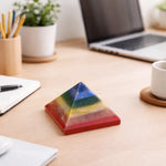 Colorful pyramid crystal on a desk with laptop, notebook, and cup in the background