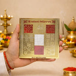 Gold-plated religious text card held by a hand with a blurred background of religious items.