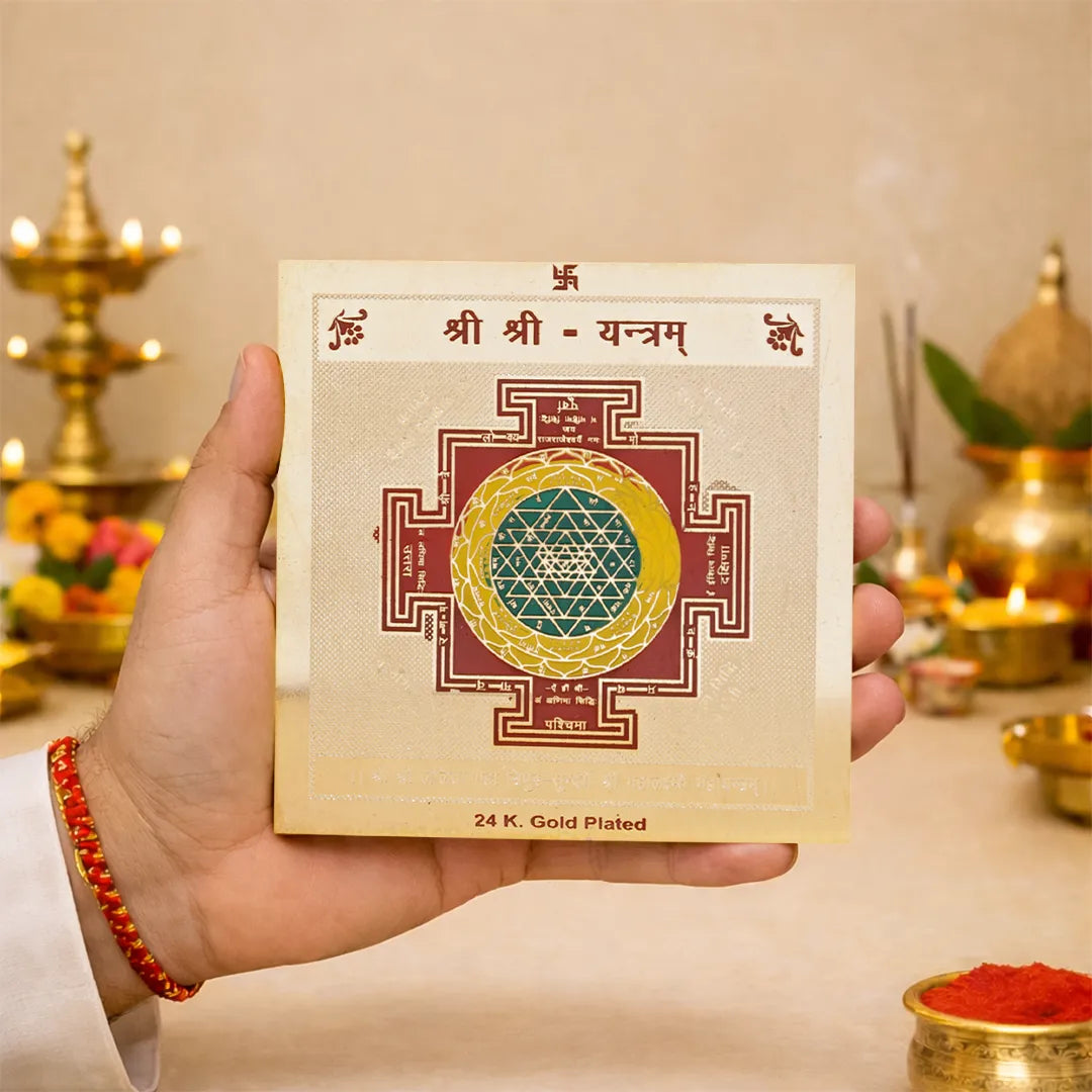 Hand holding a 24K Gold Plated Sri Yantra card with religious symbols in the background.Shree Shree Yantra – 24K Gold Plated Sacred Prosperity & Spiritual Energy Yantra