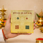 Hand holding a 24K gold-plated card with intricate designs and text, against a festive background.