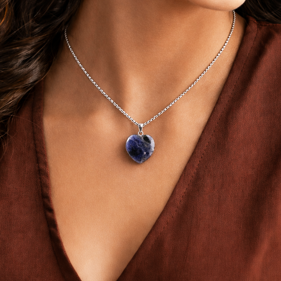 Necklace with a heart-shaped blue pendant worn by a person in a brown top.Sodalite Heart Pendant (Abhimantrit) for Clarity & Communication
