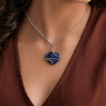 Necklace with a blue heart-shaped pendant worn by a person in a brown top.