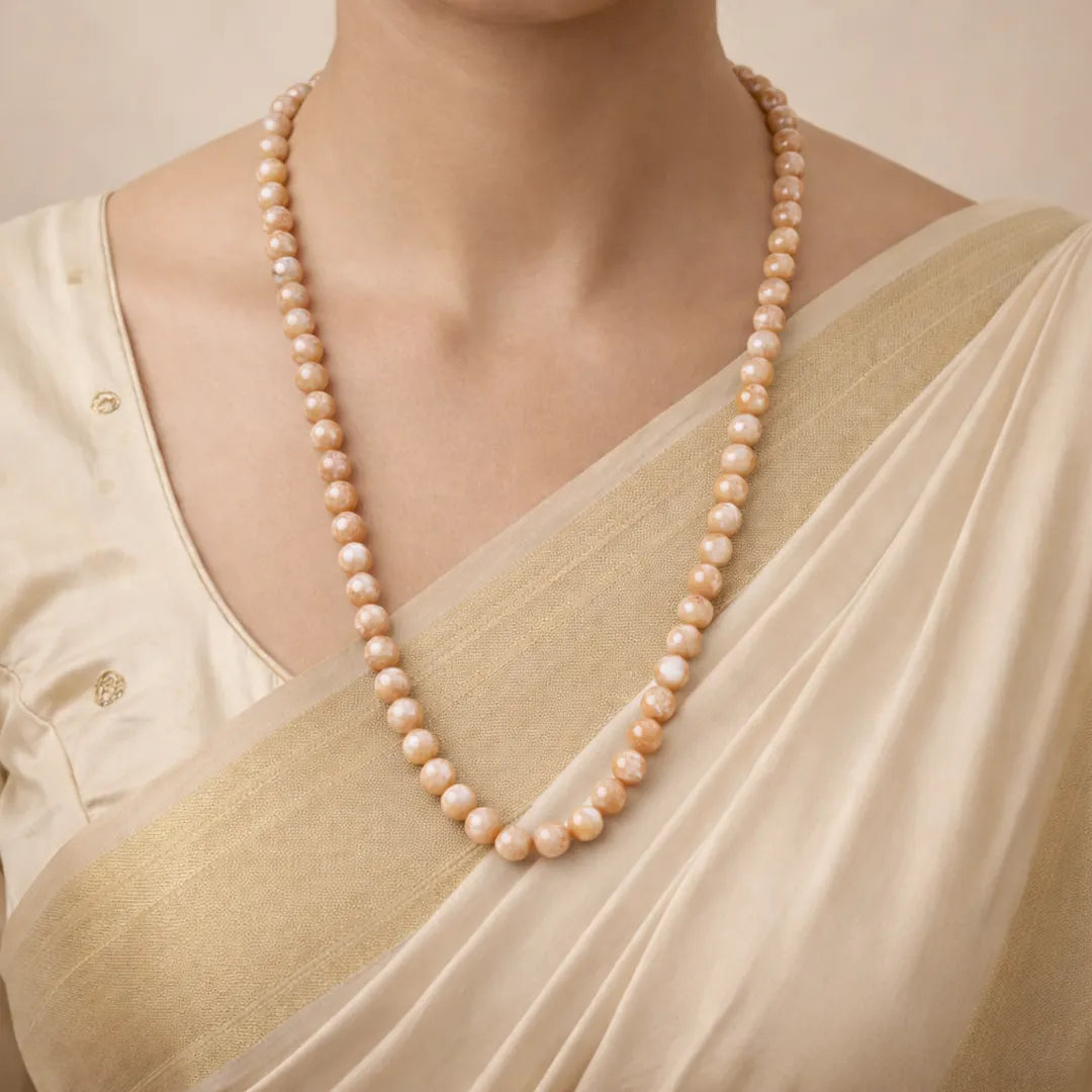 Pearl necklace worn by a person in a light-colored outfit against a neutral background