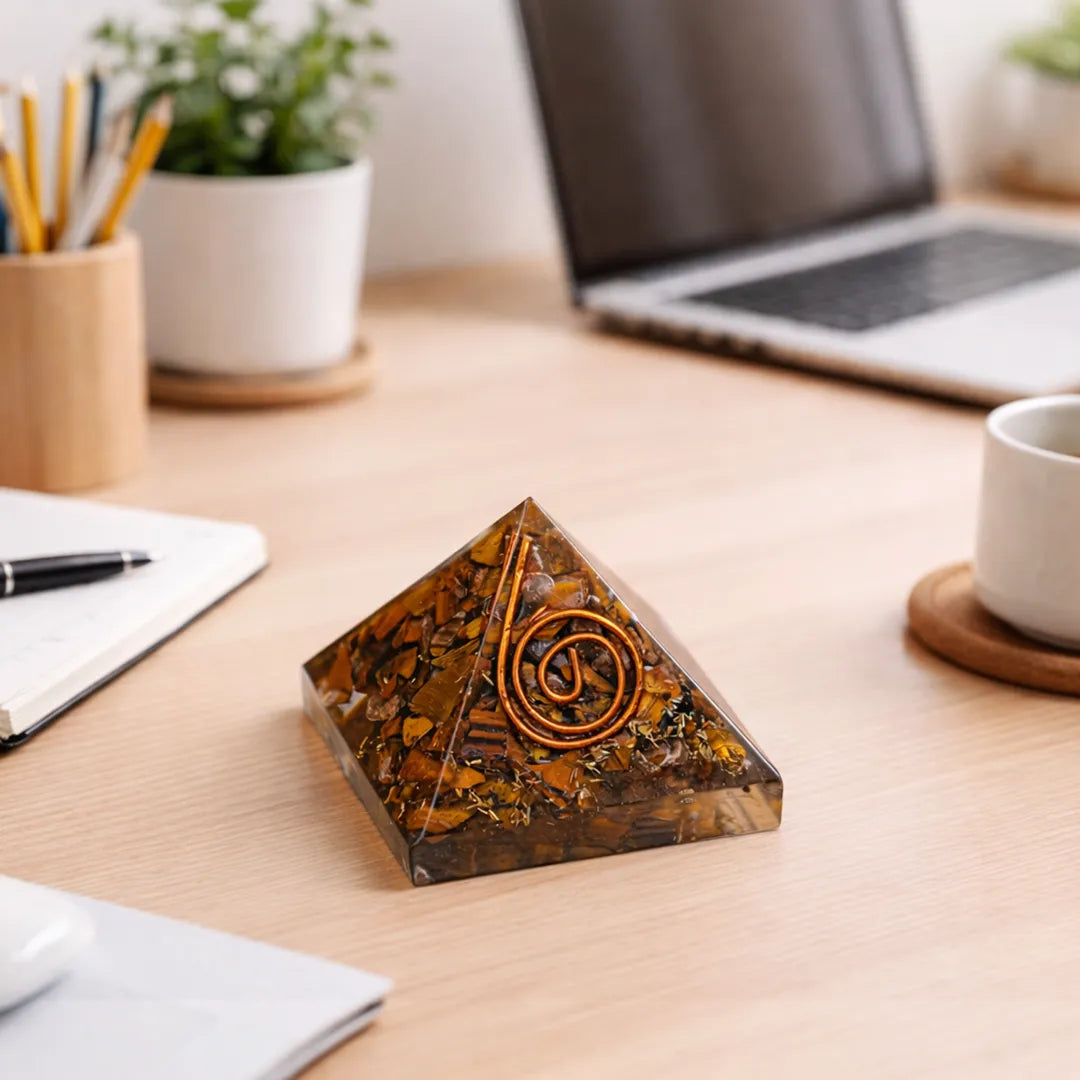 Pyramid-shaped decorative object on a desk with laptop, notebook, and cup in the backgroundTiger Eye Pyramid – Money Attraction, Protection & Confidence Crystal