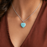 Turquoise heart-shaped pendant on a silver chain worn by a person in a brown top.