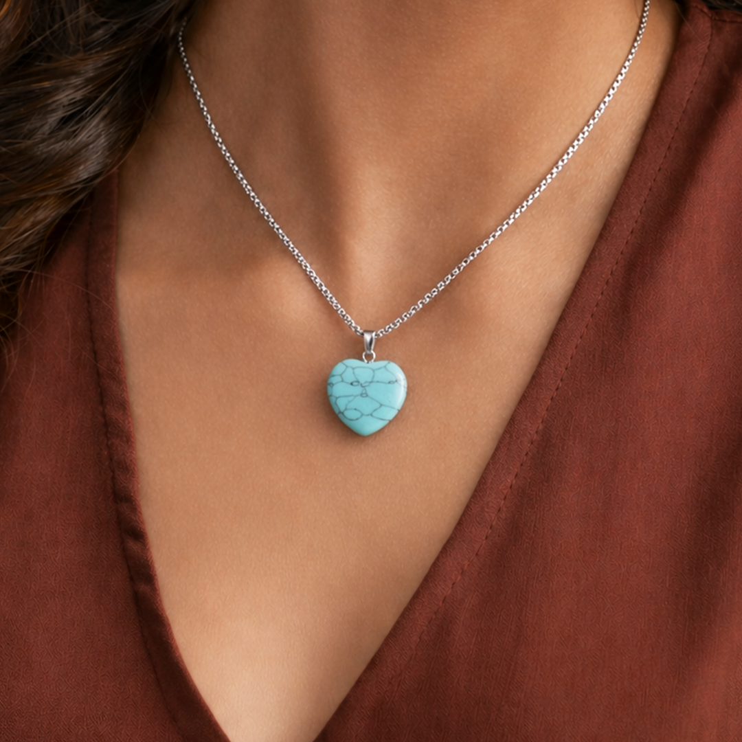 Turquoise heart-shaped pendant on a silver chain worn by a person in a brown top.Turquoise Heart Pendant (Abhimantrit) for Protection & Calmness
