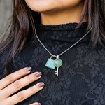 Necklace with a key and heart pendant worn by a person in a black lace top.