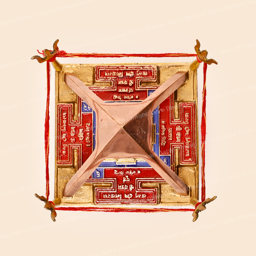 A square decorative object with a metallic gold base, red border details, blue text panels, and a central pinkish-brown geometric cross, photographed on a plain light beige background.