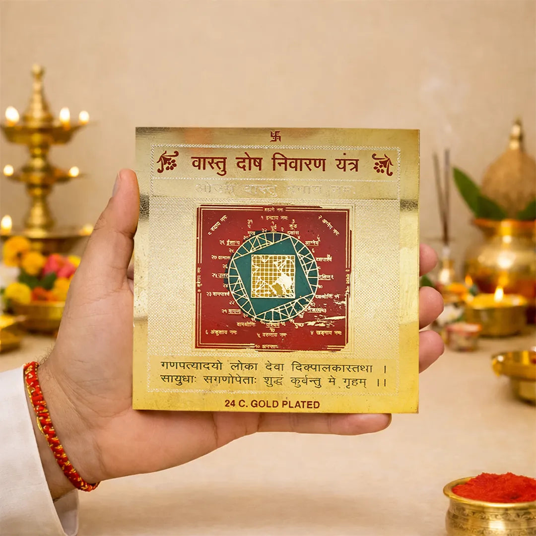 Hand holding a gold-plated astrological tool with text and design, against a blurred background of traditional decor.