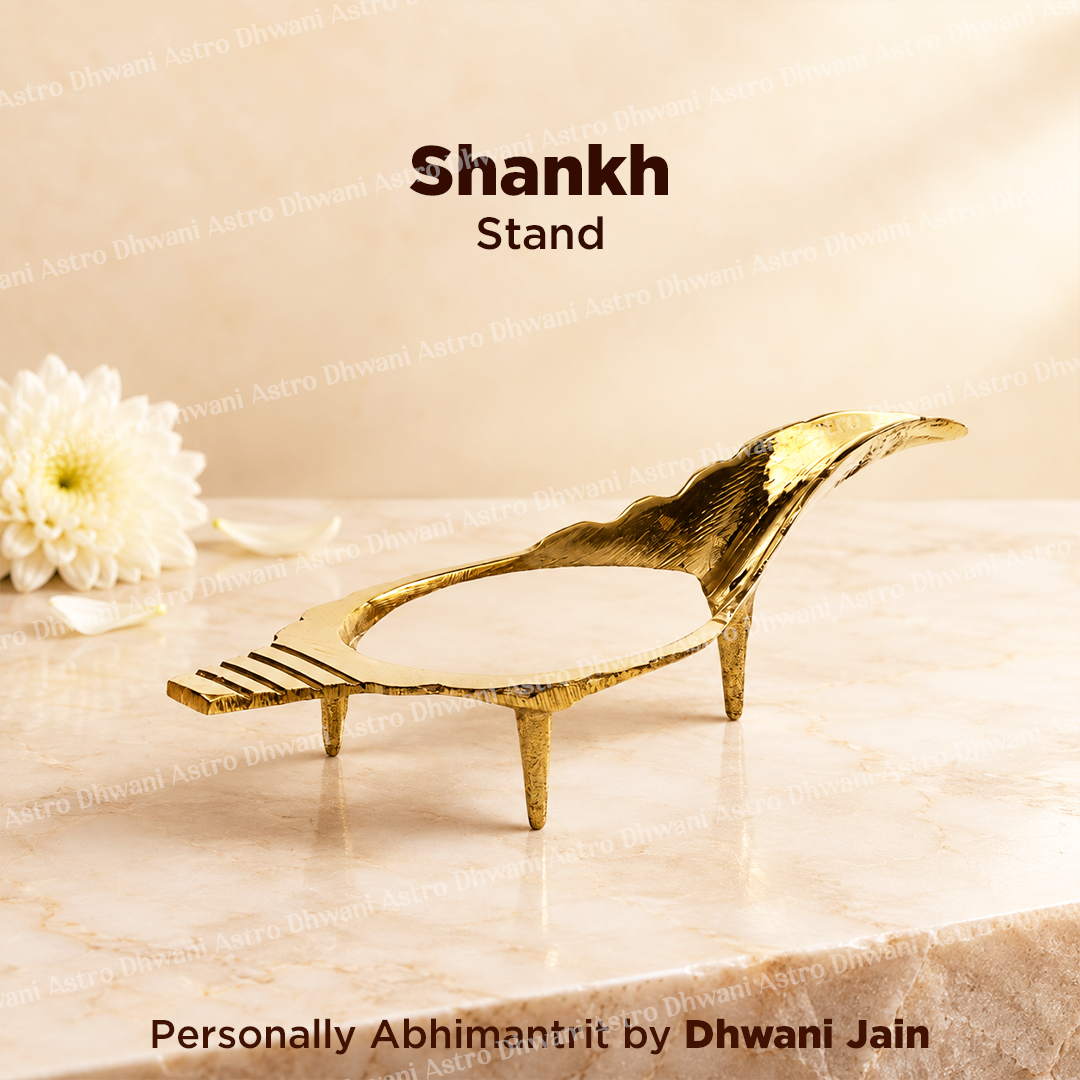 A gold-finished metal Shankh stand with a textured, organic silhouette, displayed on a beige marble surface with a white flower prop in the background.
