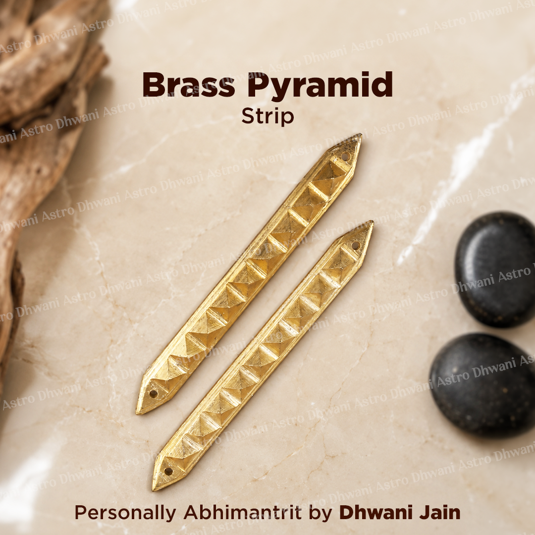 Two brass pyramid strip charms with triangular cutouts, displayed on a beige stone surface with decorative driftwood and black stones. 