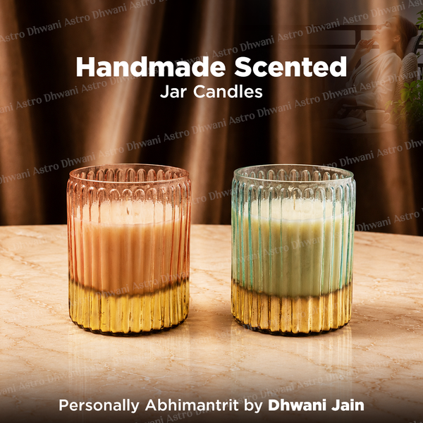 Two handmade scented jar candles in ribbed glass holders, one with a warm peach-to-gold gradient and one with a mint-to-gold gradient, displayed on a marble surface with a warm brown draped background. 