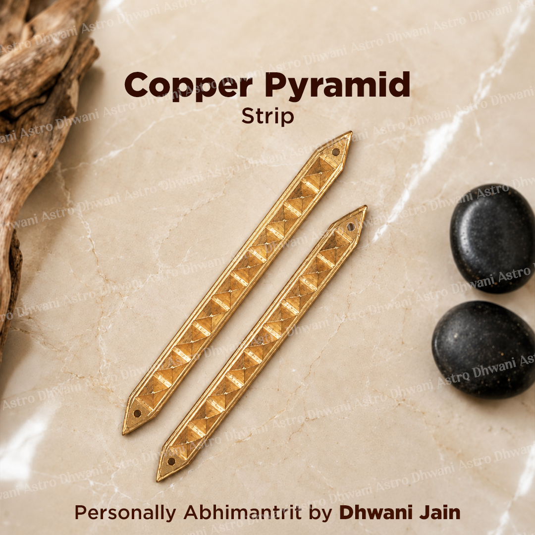 Two gold-toned copper pyramid strip charms with triangular cutouts, displayed on a beige marble surface with decorative driftwood and black stones.