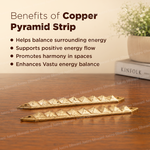Two brass pyramid strip charms displayed on a wooden table with text overlays detailing their purported benefits, alongside a potted plant and a book in the background.