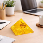 Yellow pyramid-shaped object with a spiral design on a desk with a laptop, cup, and stationery.
