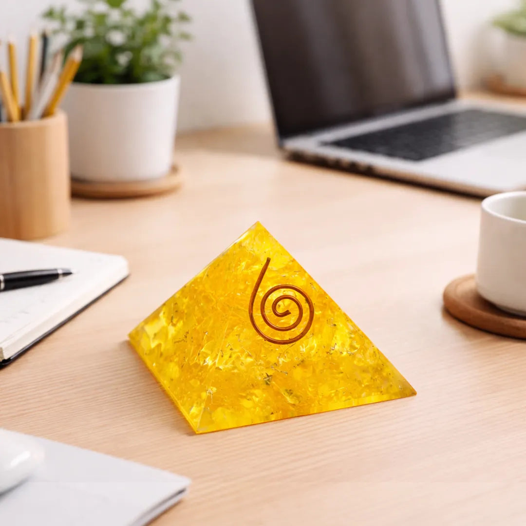 Yellow pyramid-shaped object with a spiral design on a desk with a laptop, cup, and stationery.Yellow Citrine Pyramid – Energy & Manifestation Crystal Pyramid