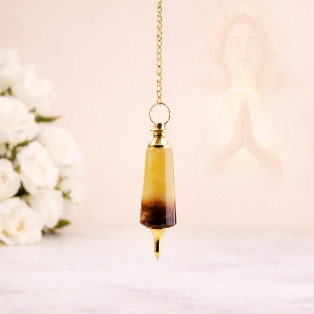 Decorative pendant with a gradient design hanging against a soft, blurred background with flowers.Yellow Quartz Pendulum for Confidence, Prosperity & Dowsing - Abhimantrit