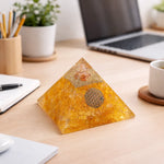 Pyramid-shaped decorative item on a desk with laptop, notebook, and cup in the background