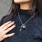 Person wearing a black lace top with a silver necklace featuring a lock and key pendant.