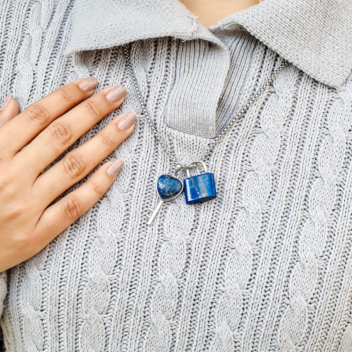 Blue padlock-shaped earrings on a gray sweater with a hand touching the collar.
