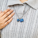 Blue padlock-shaped earrings on a gray sweater with a hand touching the collar.