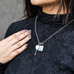 Person wearing a black lace top with a silver necklace featuring a lock and key pendant.