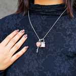 Person wearing a dark lace top with a silver necklace featuring a heart and key pendant.
