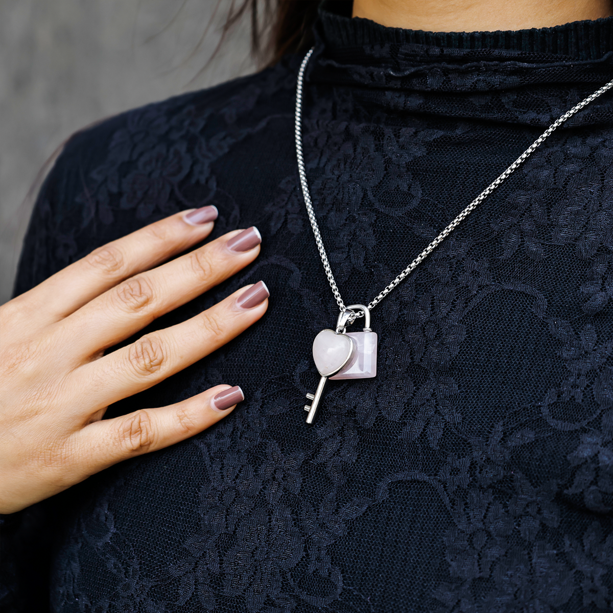 Person wearing a black lace top with a silver necklace featuring a heart and key pendant.