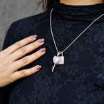Person wearing a black lace top with a silver necklace featuring a heart and key pendant.